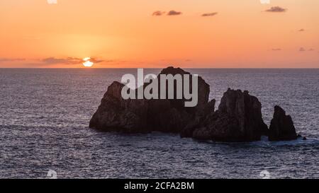 From above picturesque scenery of rough rocks among calm blue sea under colorful evening sky with sun beams breaking through clouds during twilight Costa Brava, Spain Stock Photo