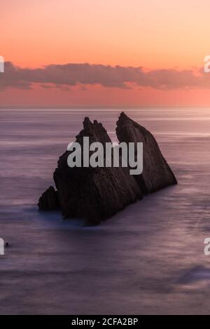 From above picturesque scenery of rough rocks among calm blue sea under colorful evening sky with sun beams breaking through clouds during twilight Costa Brava, Spain Stock Photo