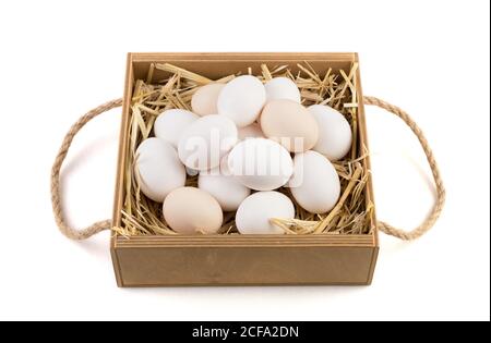 White and brown chicken eggs lie on straw in a wooden box. Stock Photo