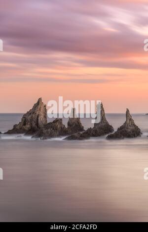 From above picturesque scenery of rough rocks among calm blue sea under colorful evening sky with sun beams breaking through clouds during twilight Costa Brava, Spain Stock Photo