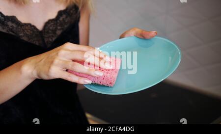 Blue plate with pink dish sponge in hand on blurred kitchen background Stock Photo