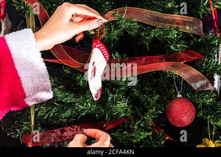 Decorating Christmas tree, hand putting Christmas decorations on fir branches. Christmas hanging decorations. Stock Photo