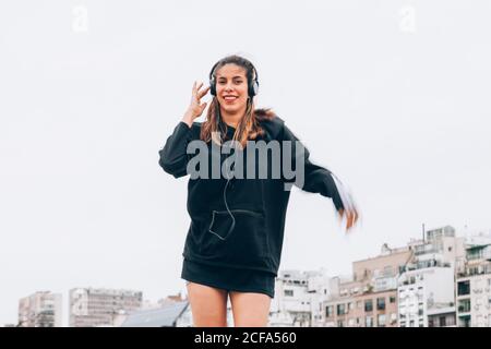 Content young Woman in casual wear dancing while using headphones at city street Stock Photo