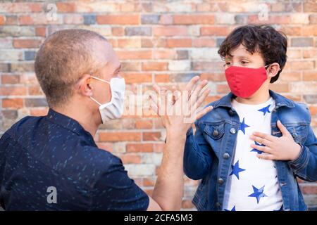 Father and son greeting each other on the street. They are wearing a face mask as a precaution for the Covid-19 pandemic. Stock Photo
