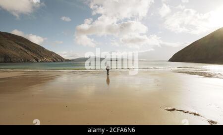 Tourist man contemplating calm nature ocean landscape while standing on sandy beach on coastline of Ireland Stock Photo