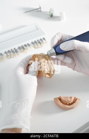 From above of crop anonymous dentist in medical gloves grinding dental prosthesis with professional tool while working in modern laboratory Stock Photo