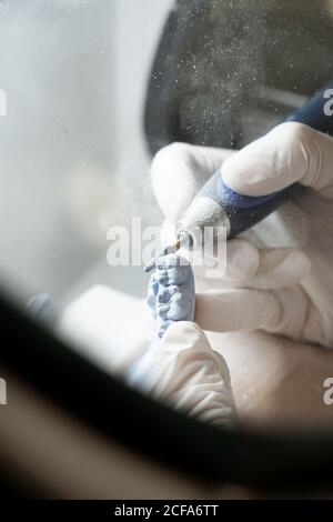 From above of crop anonymous dentist in medical gloves grinding dental prosthesis with professional tool while working in modern laboratory Stock Photo