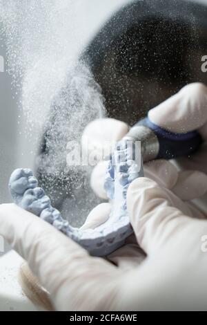 From above of crop anonymous dentist in medical gloves grinding dental prosthesis with professional tool while working in modern laboratory Stock Photo