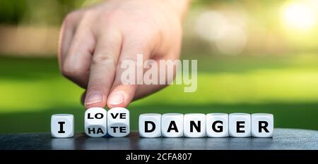 Hand turns dice and changes the expression 'I hate danger' to 'I love danger'. Stock Photo