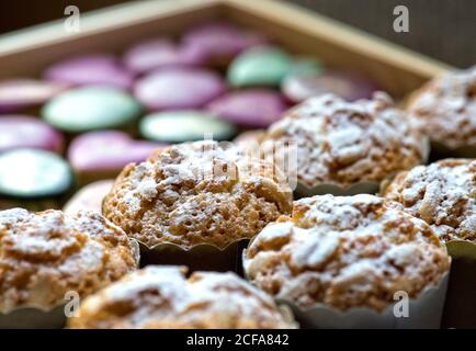 Closeup of delicious sweet muffins sprinkled with sugar powder arranged on wooden tray with assorted colorful candies Stock Photo