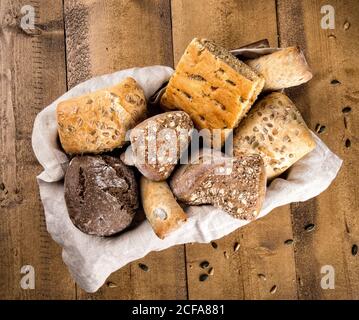 Top view of assorted bread loaves and buns made with various types of flour and grains arranged in basket on wooden table Stock Photo