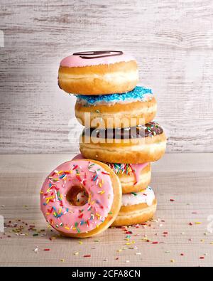 Stack of yummy sweet assorted donuts with colorful frosting and sprinkles placed on wooden background Stock Photo