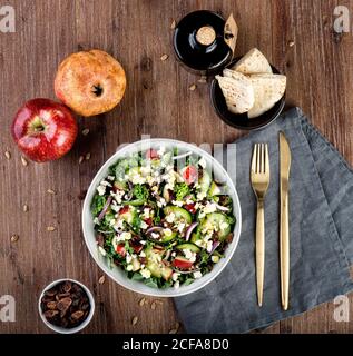 Top view of appetizing salad with chopped cucumbers and onions mixed with spinach and apples while placed on table with fork and knife Stock Photo