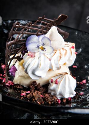 Delicious dessert made from meringue cookies decorated with violet flower and placed on plate with cream and chocolate Stock Photo