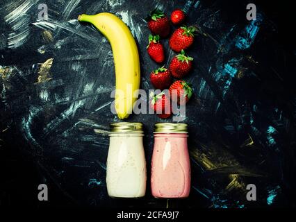 Food background, smoothies from strawberries and banana in small bottles, dark background, top view, flat lay Stock Photo