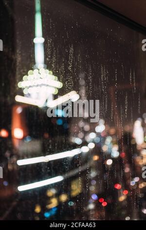 Blurred view of brightly illuminated modern city through wet window glass at rainy night in Dubai Stock Photo
