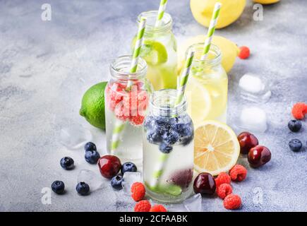 Berry and citrus fruit infused summer cold drinks in glass bottles on gray stone table background, copy space Stock Photo