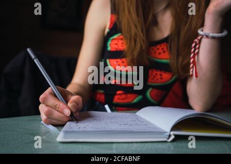 unrecognizable crop Woman sitting at table in cozy room and writing in notebook Stock Photo