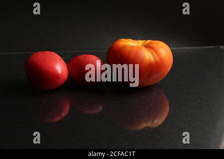 three red yellow tomatoes lie on a black background side view food background with copy space Stock Photo