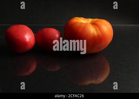 three red yellow tomatoes lie on a black background side view food background with copy space Stock Photo