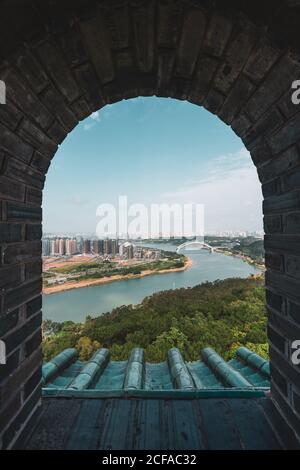 Shot through brick old window with view of cityscape of Nanning on river shore, China Stock Photo