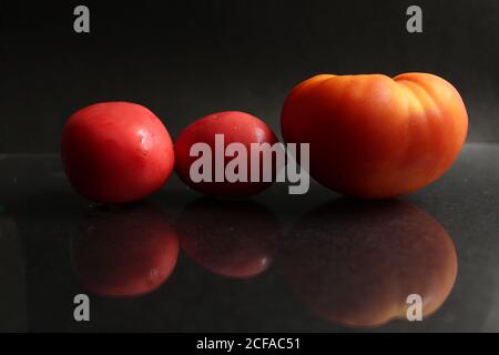 three red yellow tomatoes lie on a black background side view food background with copy space Stock Photo