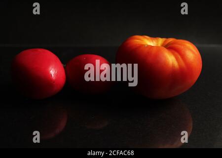 three red yellow tomatoes lie on a black background side view food background with copy space Stock Photo