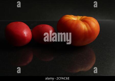 three red yellow tomatoes lie on a black background side view food background with copy space Stock Photo