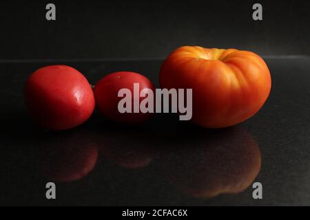 three red yellow tomatoes lie on a black background side view food background with copy space Stock Photo