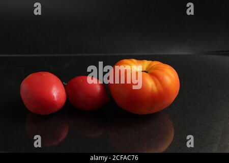 three red yellow tomatoes lie on a black background side view food background with copy space Stock Photo