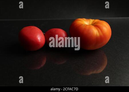 three red yellow tomatoes lie on a black background side view food background with copy space Stock Photo