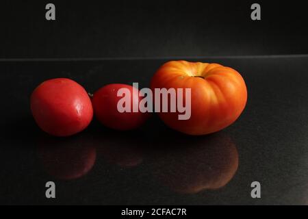 three red yellow tomatoes lie on a black background side view food background with copy space Stock Photo