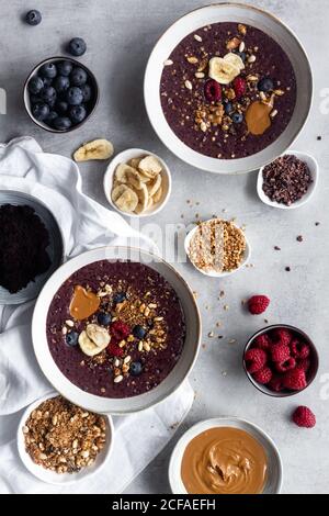 Top view composition with served for breakfast acai bowls on marble table with ingredients for recipe including nuts and cereals with fresh berries and caramel Stock Photo