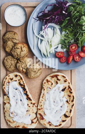 Top view of arrangement ingredients for cooking falafel and fresh vegetables and pita bread on cutting board Stock Photo