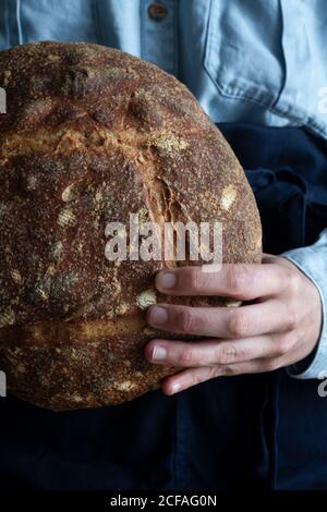 anonymous crop hand Woman in apron holding homemade sourdough bread Stock Photo