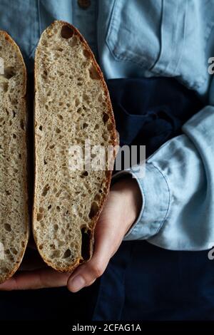 anonymous crop hand Woman in apron holding slice homemade sourdough bread and loaf of bread Stock Photo