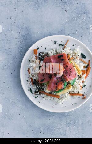 From above tasty appetizing sliced salmon on white rice with vegetables in plate on table Stock Photo