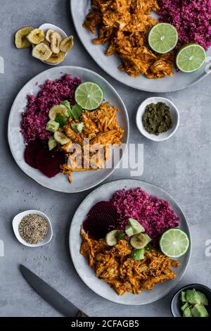 Top view of set of plates with healthy red quinoa and delicious spicy chicken curry garnished with cut lime and banana chips on grey background Stock Photo