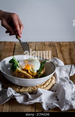 Crop anonymous hand holding dish with fried egg on potato on wooden table with fried mushrooms grated cheese and herbs Stock Photo