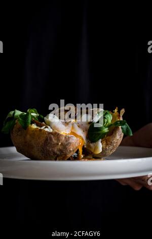 From above of white ceramic bowl with tasty fried egg mushrooms herbs in potato on crop hand Stock Photo