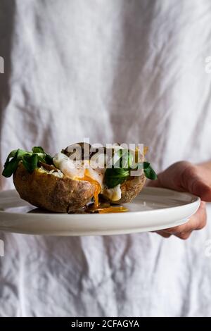 From above of white ceramic bowl with tasty fried egg mushrooms herbs in potato on crop hand Stock Photo