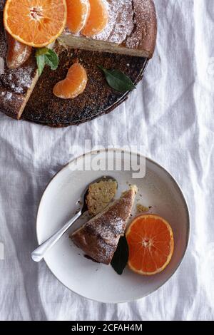From above appetizing sweet cake and ripe orange mandarin cut and served on white plate on table Stock Photo