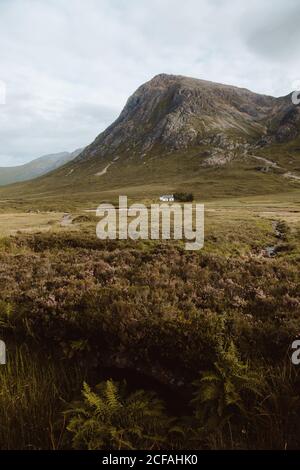 Picturesque view of white building and trees in middle of green valley by high rocks in Glencoe on daytime Stock Photo