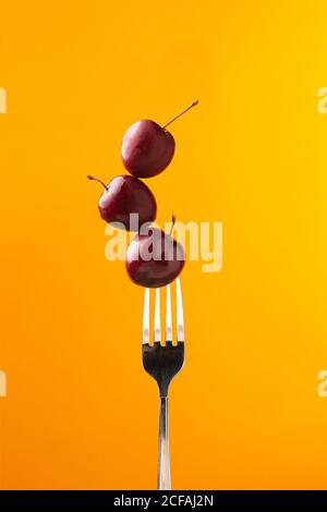 Composition of tasty juicy cherries and fork on bright yellow background Stock Photo