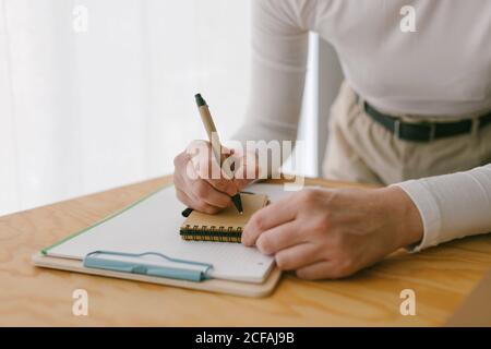 faceless casual businessWoman bending on wooden table and writing in notepad with pen Stock Photo