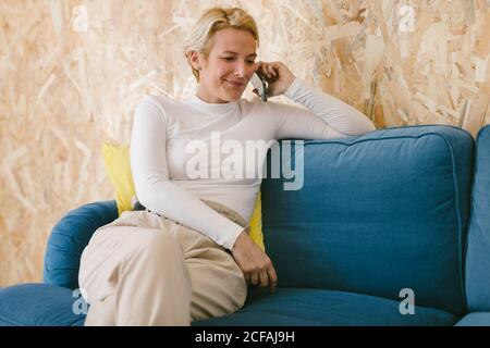 Adult businessWoman with short hairstyle sitting in leisure on sofa and browsing mobile phone in office Stock Photo