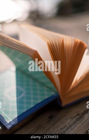 From above closeup of opened book with yellow pages and blue cover placed on wooden bench in sunny day Stock Photo