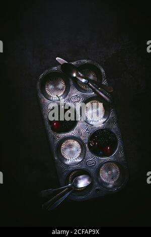 From above tasty fragrant ripe blackberry and cherry in steel shape with knife and spoon on black background Stock Photo