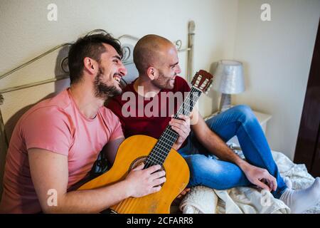 gay couple playing the guitar in the bedroom Stock Photo