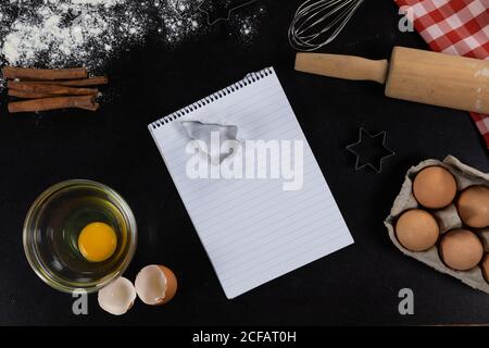 View of an empty notebook page with ingredients prepared for baking cookies, arranged on a plain bla Stock Photo